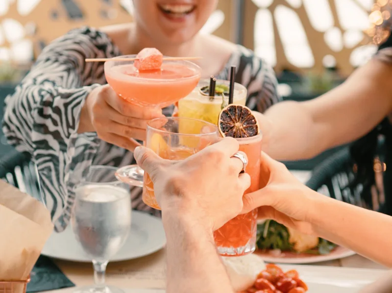 Four hands toasting with cocktails over a table