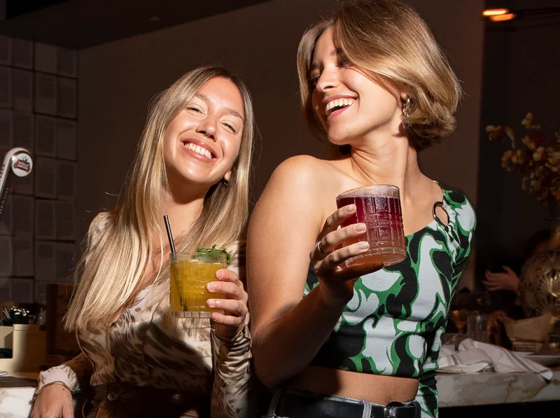 Two guests laughing with cocktails in hand at the bar